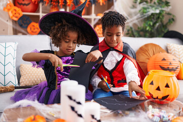 Fototapeta premium Adorable african american boy and girl having halloween party cutting paper at home
