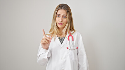 Young blonde woman doctor standing with serious expression saying no with finger over isolated white background