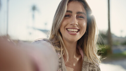 Young blonde woman smiling confident making selfie by camera at street