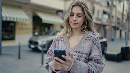 Young blonde woman using smartphone with relaxed expression at street