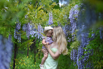 woman and her little daughter posing in spring park with wisteria flowers