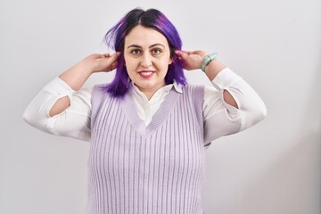 Plus size woman wit purple hair standing over white background smiling pulling ears with fingers,...