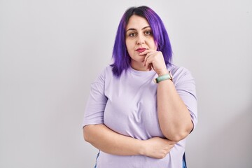 Plus size woman wit purple hair standing over isolated background looking confident at the camera with smile with crossed arms and hand raised on chin. thinking positive.