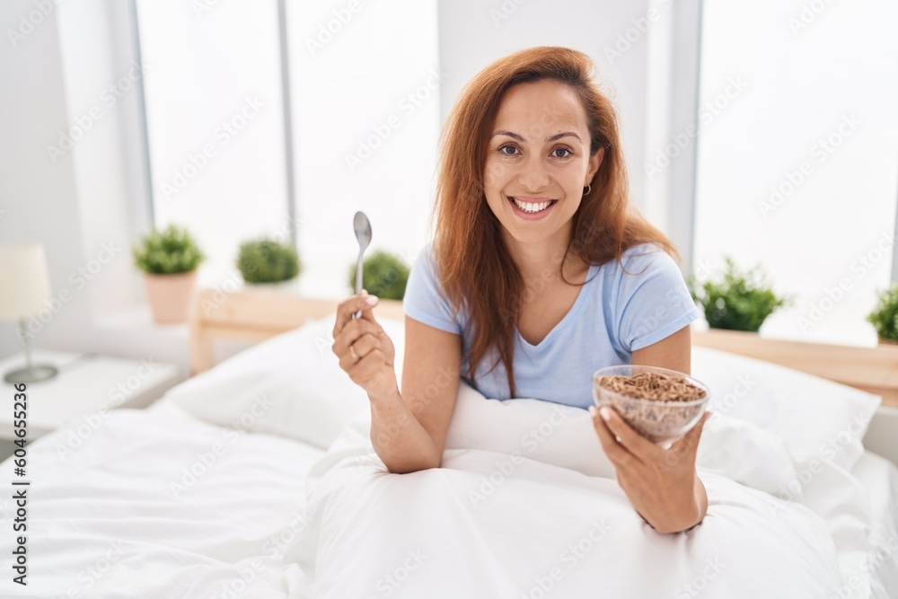 Poster brunette woman eating breakfast in the bed smiling with a happy and cool smile on face. showing teet