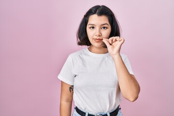 Young hispanic woman wearing casual white t shirt over pink background mouth and lips shut as zip with fingers. secret and silent, taboo talking