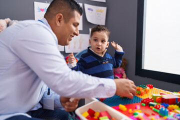 Hispanic man and boy playing with construction blocks sitting on table at kindergarten