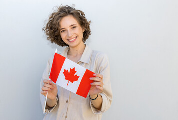 Smiling happy woman hold UK Canada flag, looking camera on gray wall background. Canadian education.