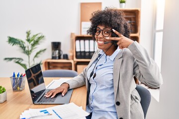 Black woman with curly hair wearing call center agent headset at the office doing peace symbol with...