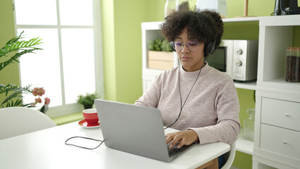 Young african american woman using laptop and headphones sitting on table at home