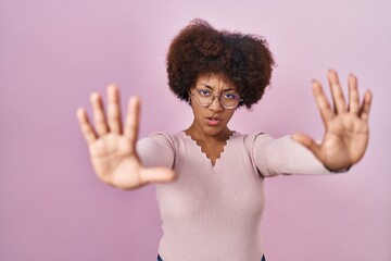 Young african american woman standing over pink background doing stop gesture with hands palms, angry and frustration expression