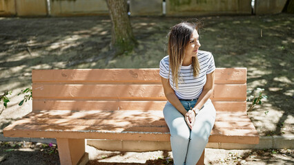 Middle eastern woman looking around with serious expression sitting on bench alone at street
