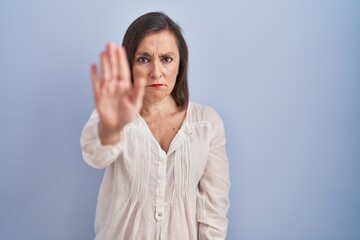 Middle age hispanic woman standing over blue background doing stop sing with palm of the hand....