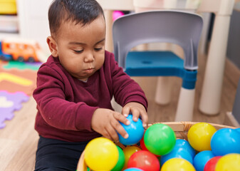 Fototapeta na wymiar Adorable hispanic boy playing with balls sitting on floor at kindergarten