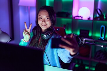 Young chinese woman streamer smiling confident make selfie by smartphone at gaming room