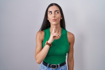 Young woman standing over isolated background thinking concentrated about doubt with finger on chin...