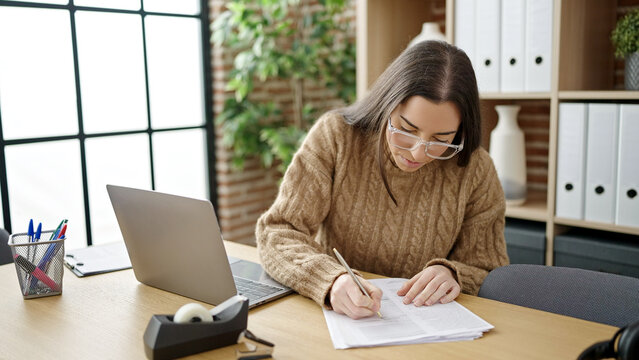 Young beautiful hispanic woman business worker using laptop writing on document at office