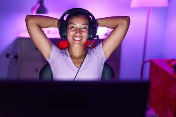 Young beautiful hispanic woman streamer playing video game relaxed with hands on head at gaming room