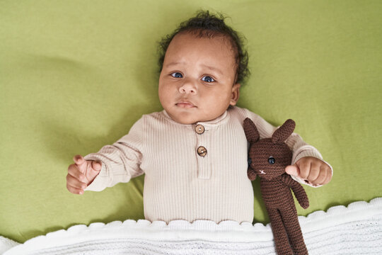 African american baby relaxing on bed with doll at bedroom