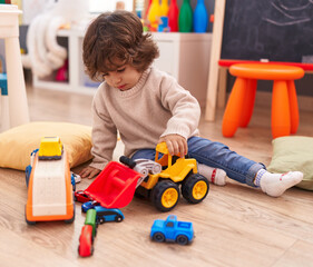 Adorable hispanic boy playing with car toy sitting on floor at kindergarten