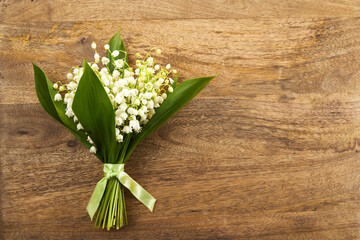 Lily of the valley flowers on wooden background. Beautiful bouquet of white flowers with green leaves.