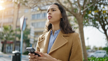 Young beautiful hispanic woman using smartphone with serious face at park