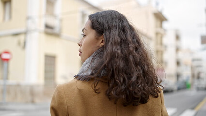 Young beautiful hispanic woman standing backwards with serious expression at street