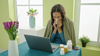 Young beautiful hispanic woman using laptop sitting on the table being sick at home