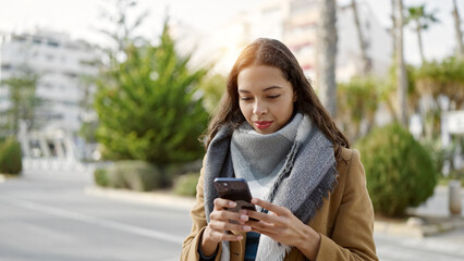 Young beautiful hispanic woman using smartphone smiling at street