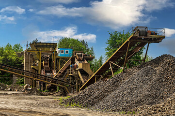 Fototapeta premium Crushing machinery, cone type rock crusher, conveying crushed granite gravel stone in a quarry open pit mining. Minning industry gravel quarry conveyor.