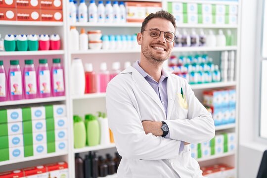 Young hispanic man pharmacist smiling confident standing with arms crossed gesture at pharmacy
