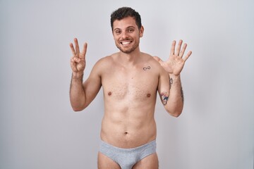 Fototapeta premium Young hispanic man standing shirtless wearing underware showing and pointing up with fingers number eight while smiling confident and happy.