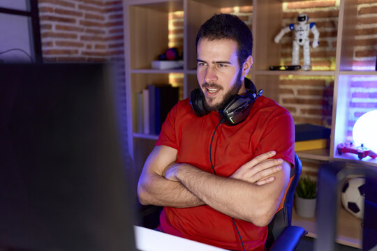Young hispanic man streamer smiling confident sitting with arms crossed gesture at gaming room