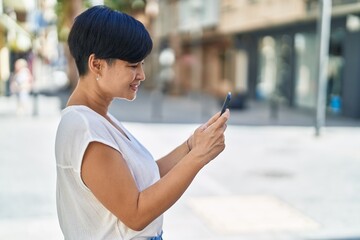 Middle age chinese woman smiling confident using smartphone at street