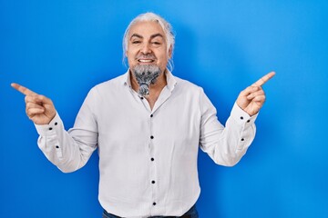 Middle age man with grey hair standing over blue background smiling confident pointing with fingers to different directions. copy space for advertisement