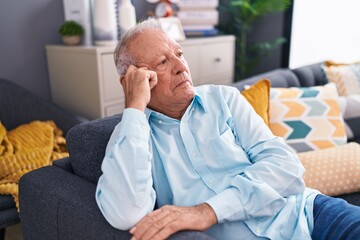 Fototapeta premium Middle age grey-haired man sitting on sofa with serious expression at home