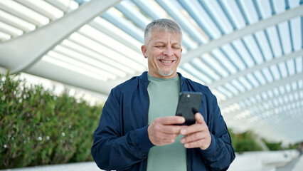 Middle age grey-haired man smiling confident using smartphone at park