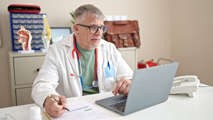 Fototapeta na wymiar Middle age grey-haired man doctor using laptop working at clinic