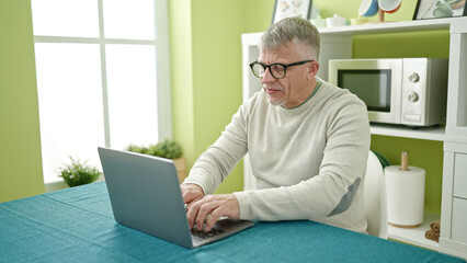 Middle age grey-haired man using laptop sitting on table at home