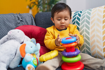 Adorable hispanic boy playing with hoops game sitting on sofa at home