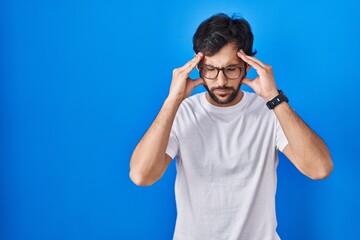 Fototapeta premium Handsome latin man standing over blue background with hand on head for pain in head because stress. suffering migraine.