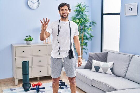 Handsome latin man wearing sportswear at home showing and pointing up with fingers number four while smiling confident and happy.