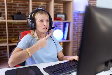 Young caucasian woman playing video games wearing headphones pointing aside worried and nervous with forefinger, concerned and surprised expression