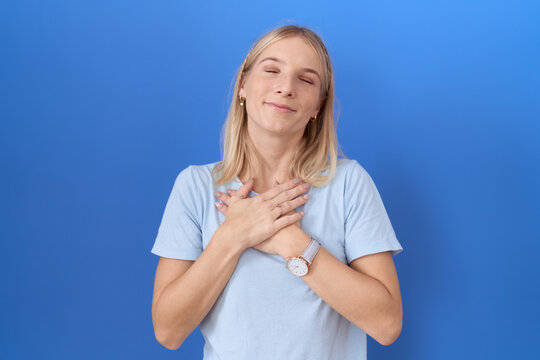 Young caucasian woman wearing casual blue t shirt smiling with hands on chest with closed eyes and grateful gesture on face. health concept.