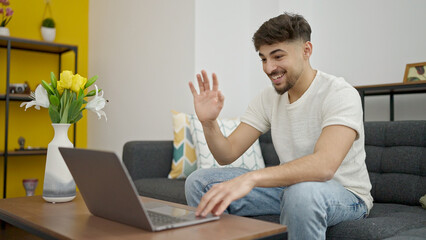 Young arab man having video call sitting on sofa at home
