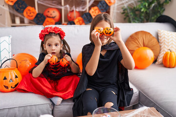Fototapeta premium Adorable boy and girl wearing halloween costume holding pumpkin baskets over eyes at home