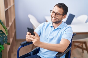 Young man using smartphone sitting on wheelchair at home