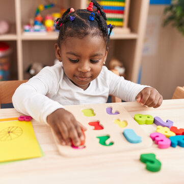 African american girl playing with maths puzzle game sitting on table at kindergarten
