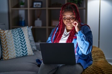 African american woman with braided hair using computer laptop at night mouth and lips shut as zip...