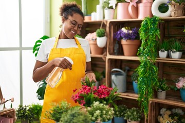 African american woman florist using diffuser watering plant at flower shop