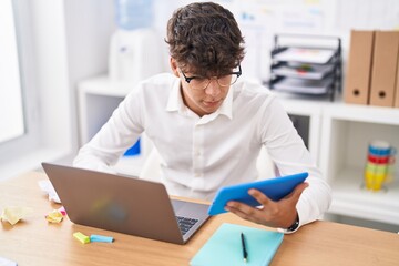 Young hispanic teenager business worker using touchpad and laptop at office